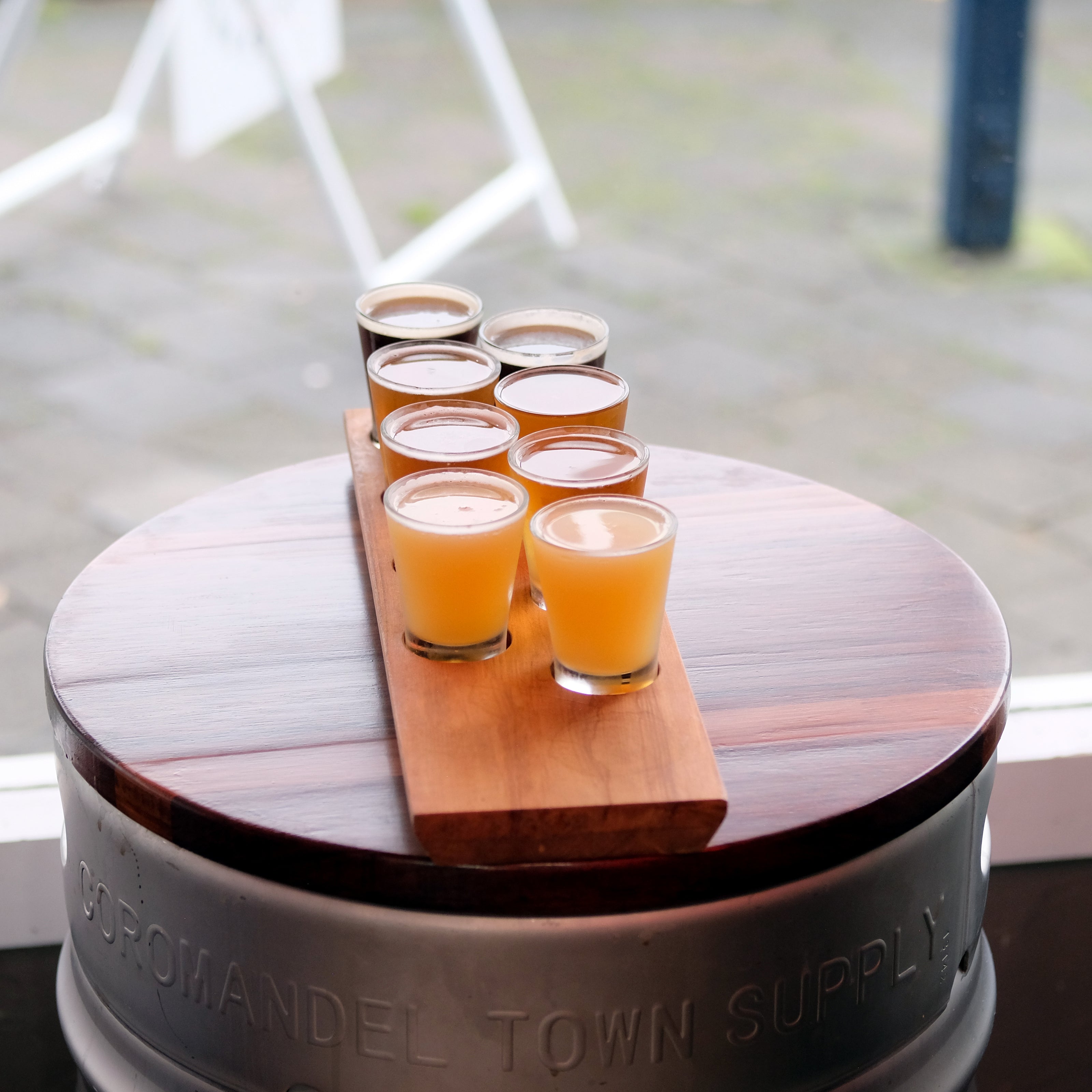 Set of six beer glasses on a wooden board with 'Coromandel Town Supply' branding.